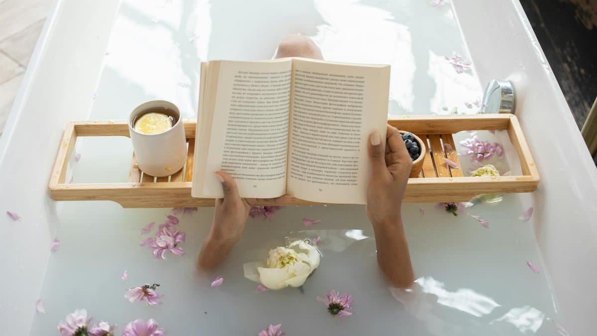 Enjoy a tranquil bath with a book surrounded by flowers and warm tea. Perfect spa day setting.