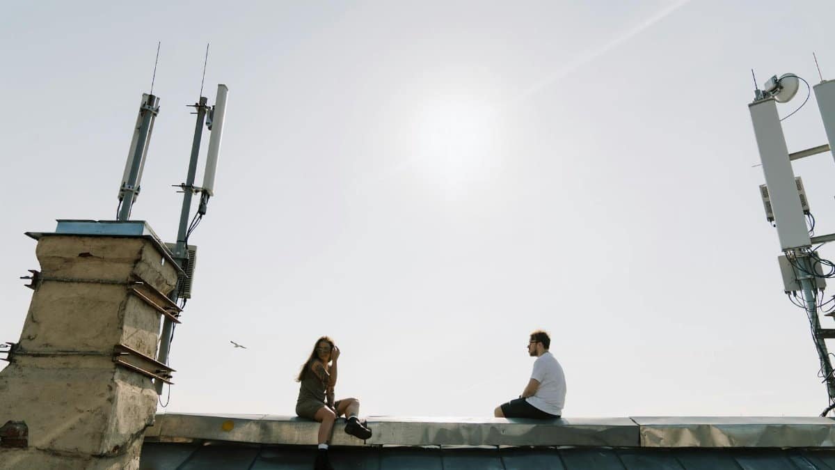 Two people enjoying leisure time on a rooftop with clear sky and urban antennas.