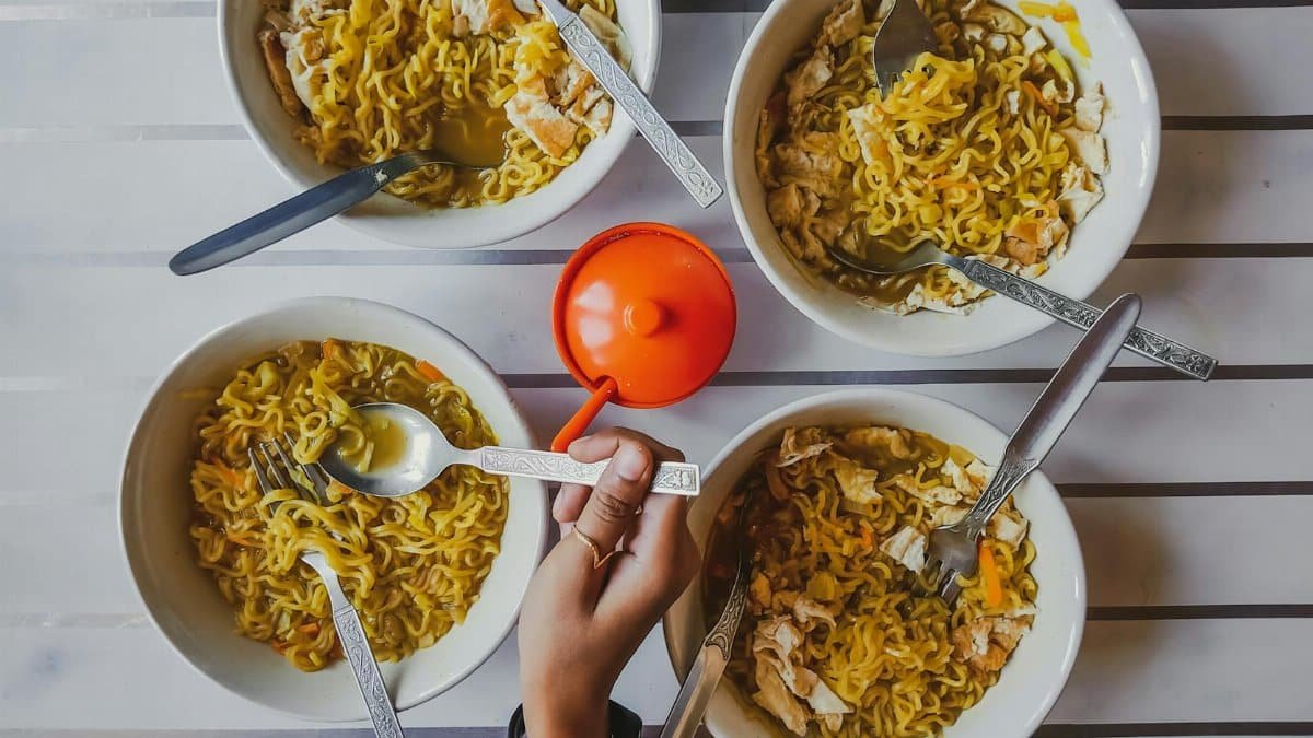 An overhead shot featuring multiple bowls of noodles with a hand reaching in, showcasing a communal meal.