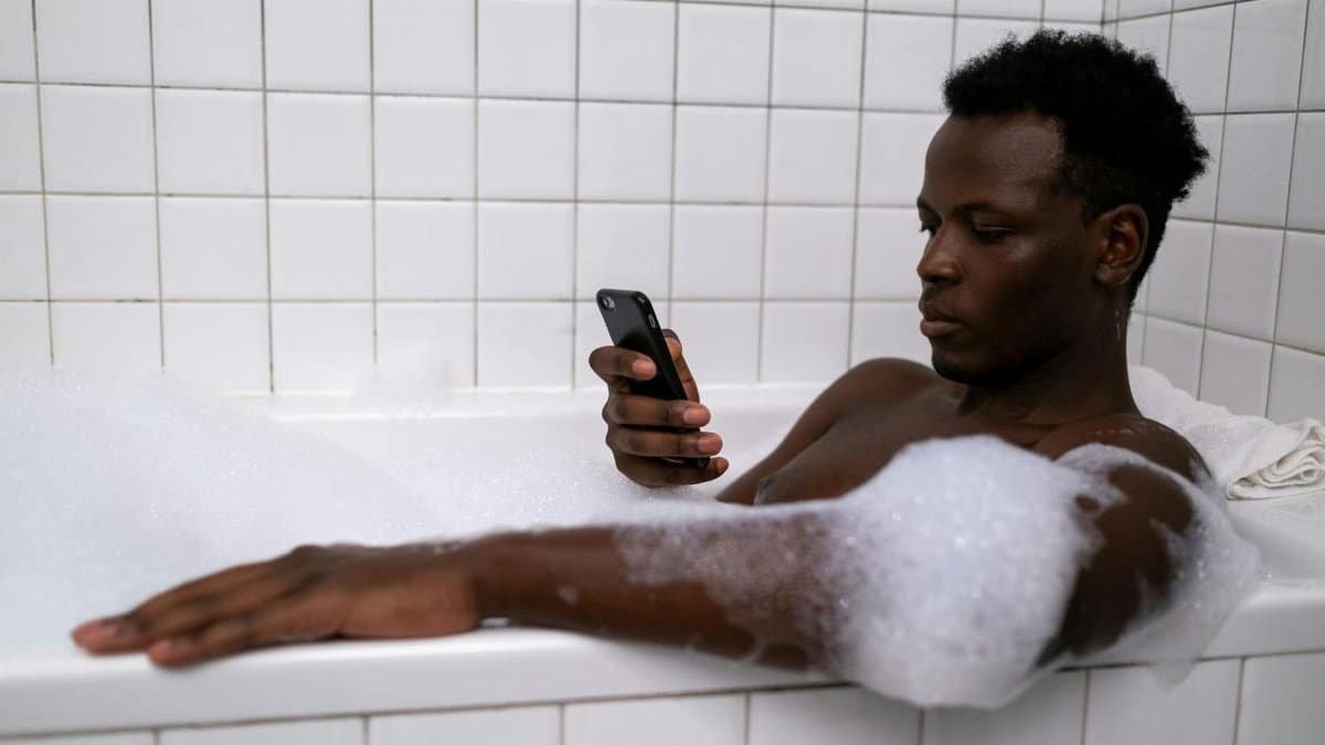 An adult man enjoys a relaxing bath while using a mobile phone, focusing on personal time and technology.