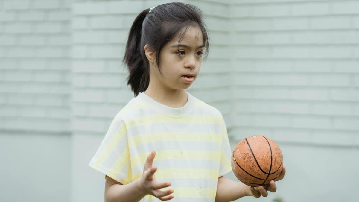 A young girl with Down syndrome holding a basketball outdoors.