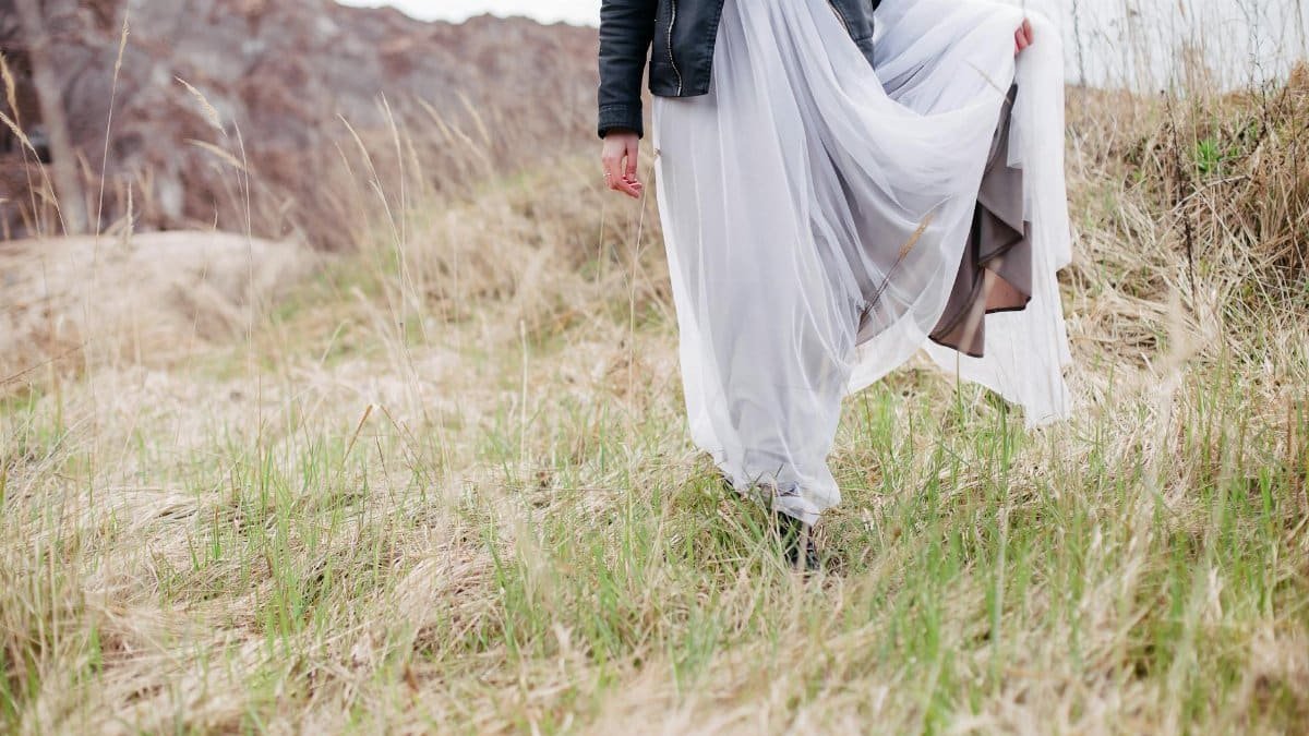 A woman in a flowing dress walking gracefully through a grassy field.