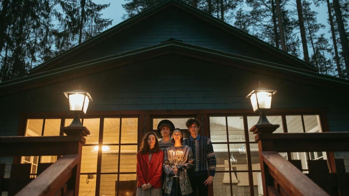 A group of friends celebrating Hanukkah with a menorah on a cabin porch.
