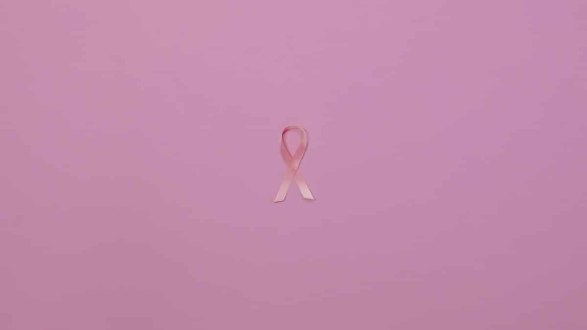 Pink ribbon on pastel background symbolizing breast cancer awareness.