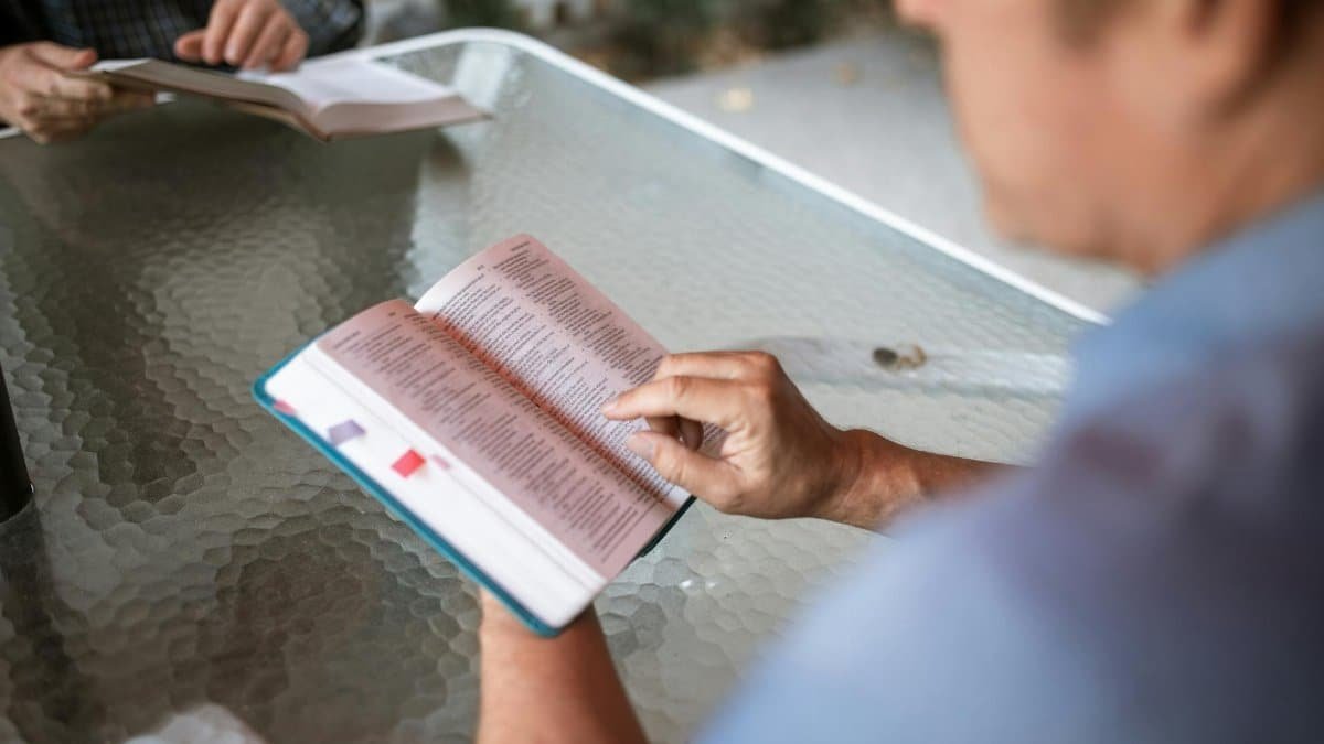 Two adults engaged in Bible study at a glass table outdoors, promoting faith and connection.