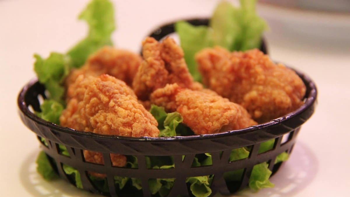 Close-up of crispy fried chicken served in a black basket with fresh lettuce, highlighting food texture.