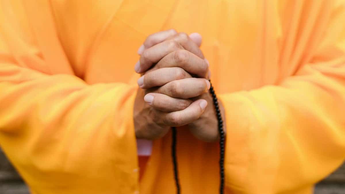 Close-up of hands in prayer wearing yellow robes, sign of Zen meditation and peace.