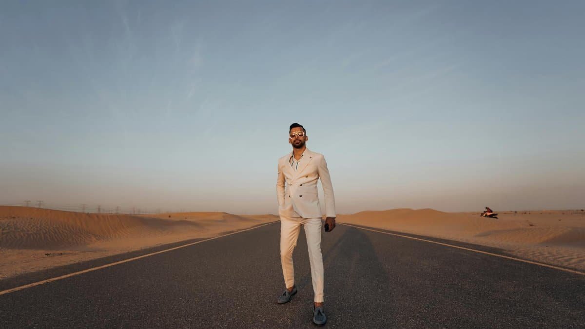 Elegant man in formal wear standing on a desert road during sunset, exuding confidence and style.