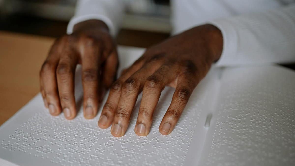 A close-up shot of hands reading a Braille book, highlighting visual impairment and accessibility.