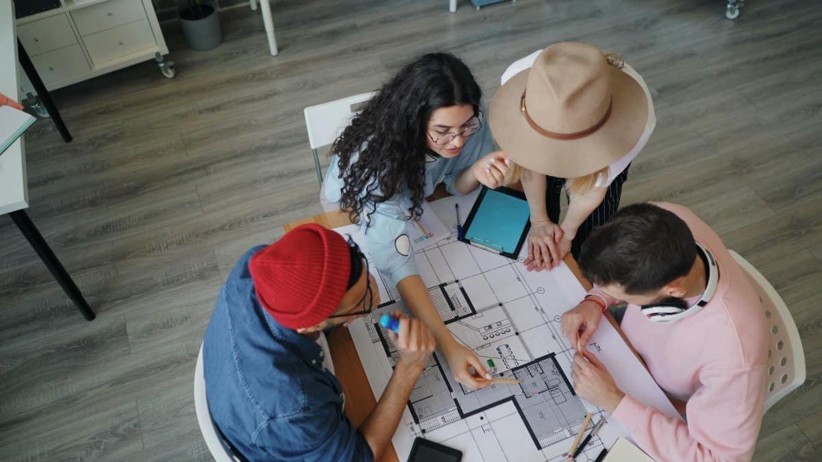 Four people collaborating over architectural blueprints in a modern office setting.
