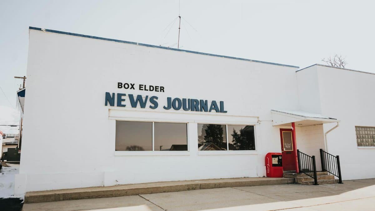 Exterior view of Box Elder News Journal building with red door and sign.