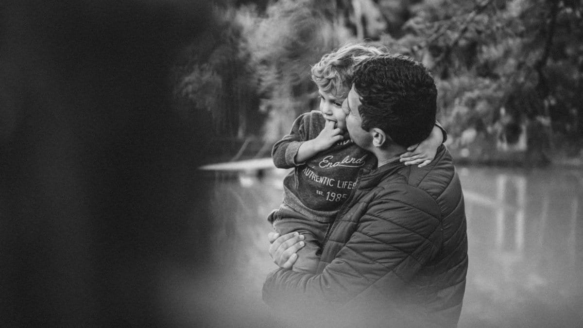 A touching black and white image of a father lovingly holding his son amid nature.