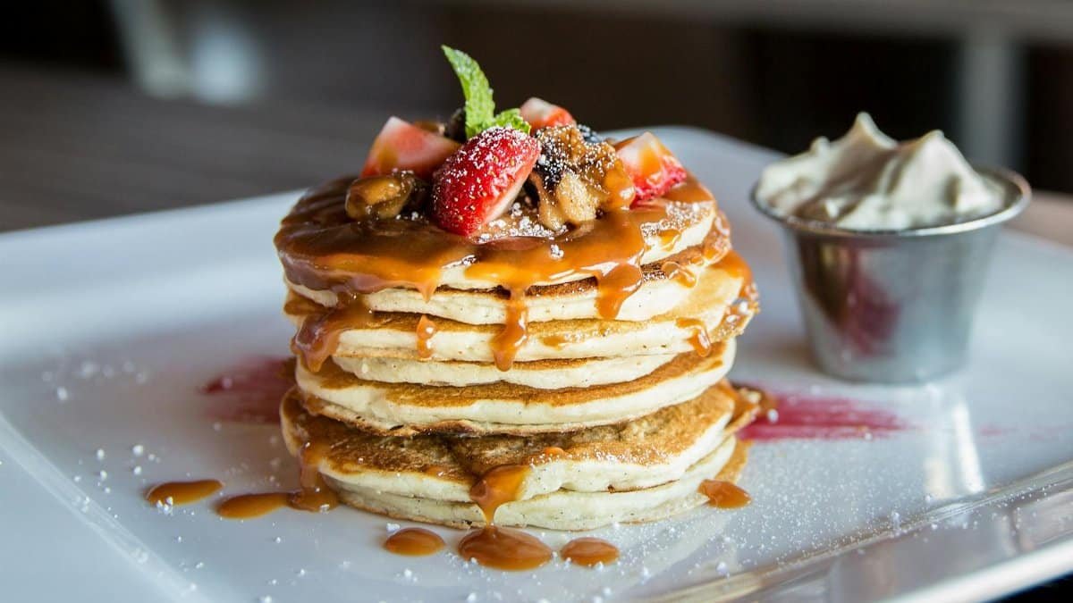 Mouthwatering pancakes with strawberries, nuts, and syrup on a plate.