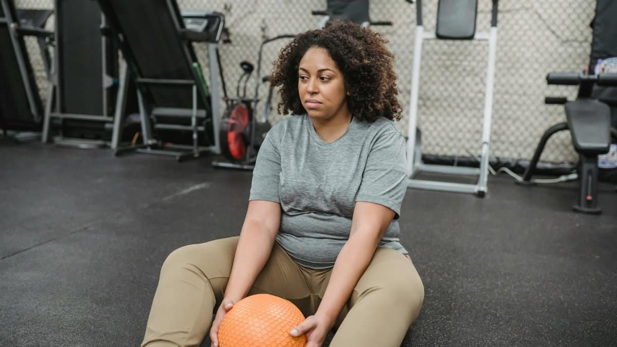 A plus size woman takes a break at the gym, holding an exercise ball, symbolizing determination and wellness.