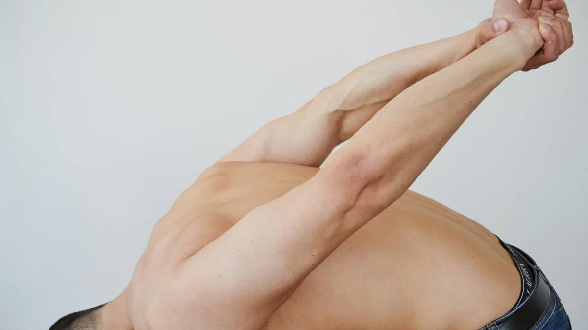 Close-up of a shirtless man stretching indoors, focusing on flexibility and muscle toning.