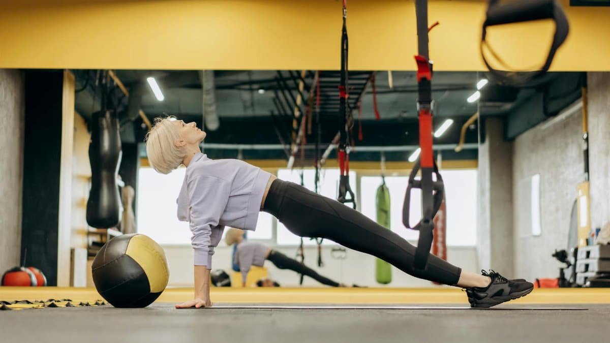 Female athlete practicing Pilates with a medicine ball in a modern gym setting.