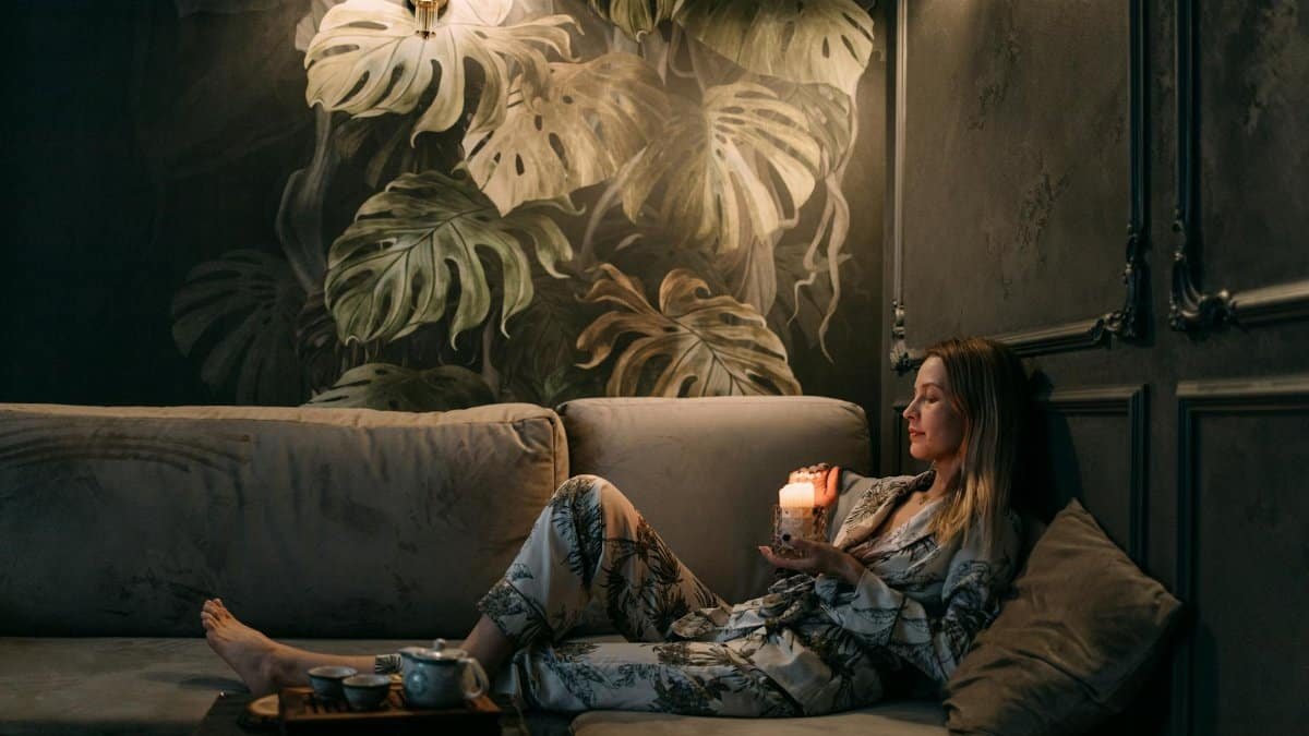 A woman relaxes on a sofa with a candle, creating a calming atmosphere indoors.