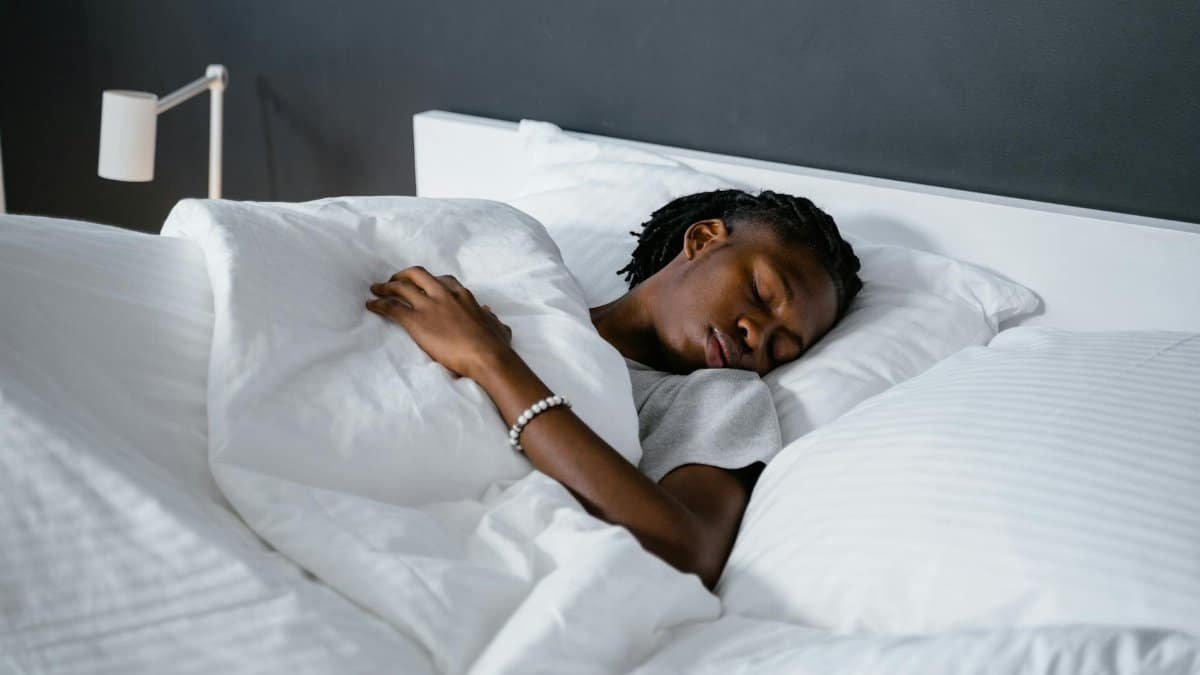 A man sleeping peacefully under a white blanket in a cozy bedroom.
