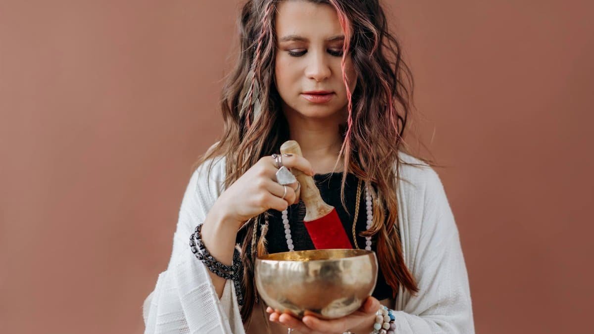 A woman focuses in meditation using a Tibetan singing bowl, promoting healing and mindfulness.