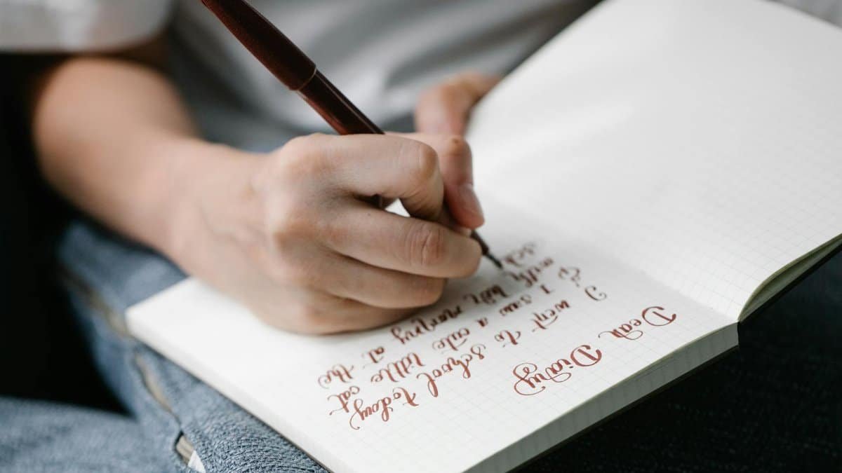 Person writing in a notebook with elegant handwritten calligraphy.