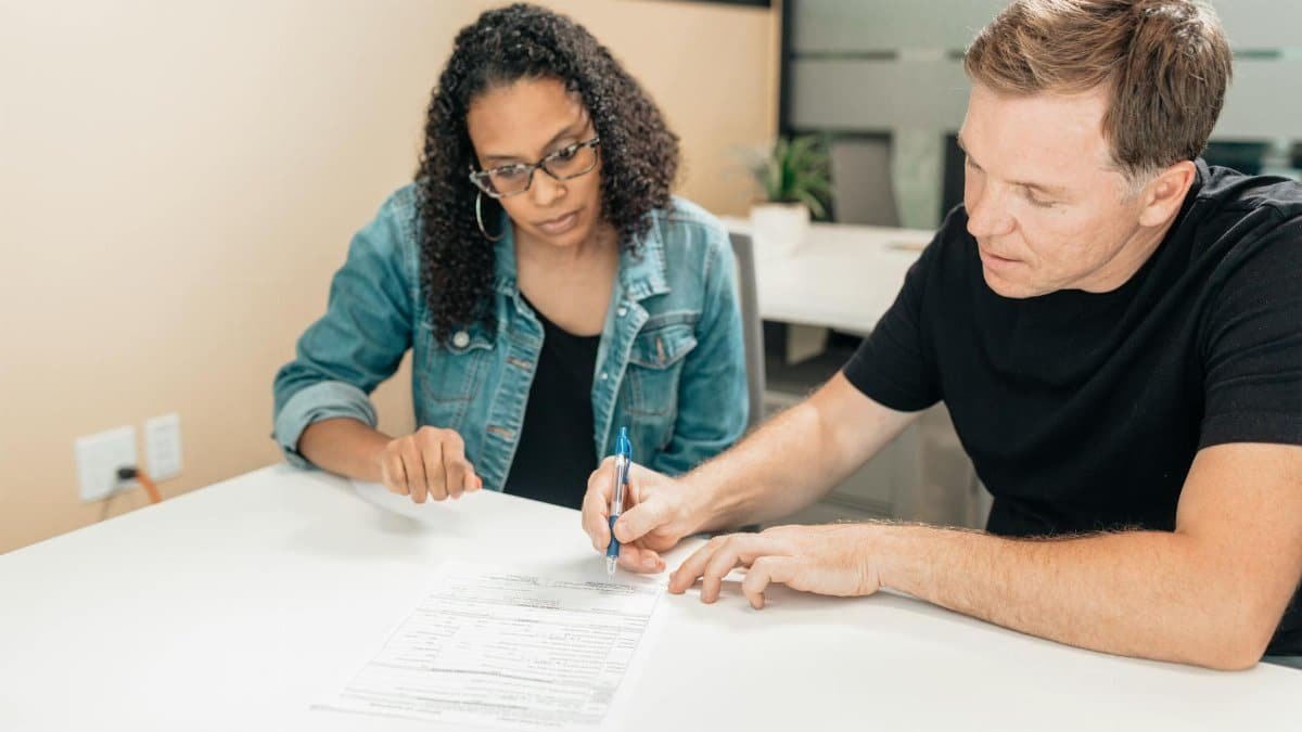 A couple working together to sign important legal documents at a desk in an office setting.