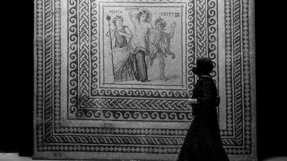 A woman in deep thought at a museum, viewing a detailed mosaic art piece in black and white.