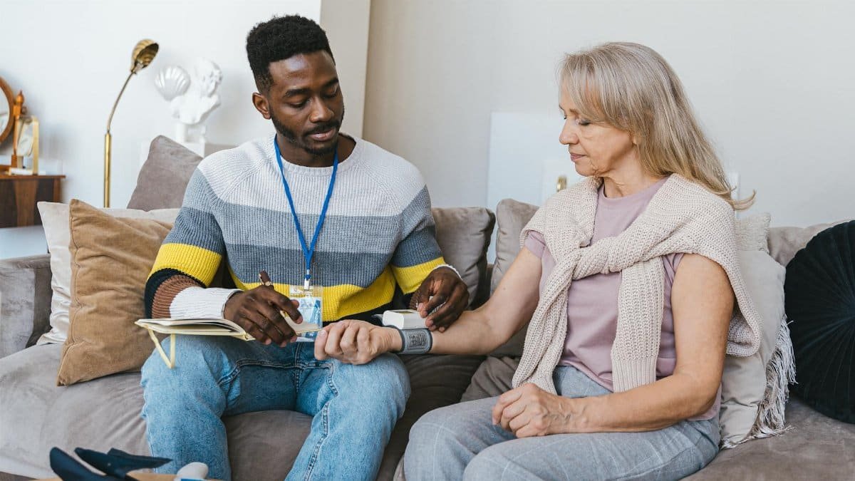 Volunteer checking elderly woman's blood pressure at home. Compassionate healthcare support.