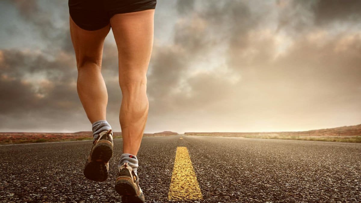 Runner's legs on a road during a sunset, symbolizing endurance and outdoor fitness training.