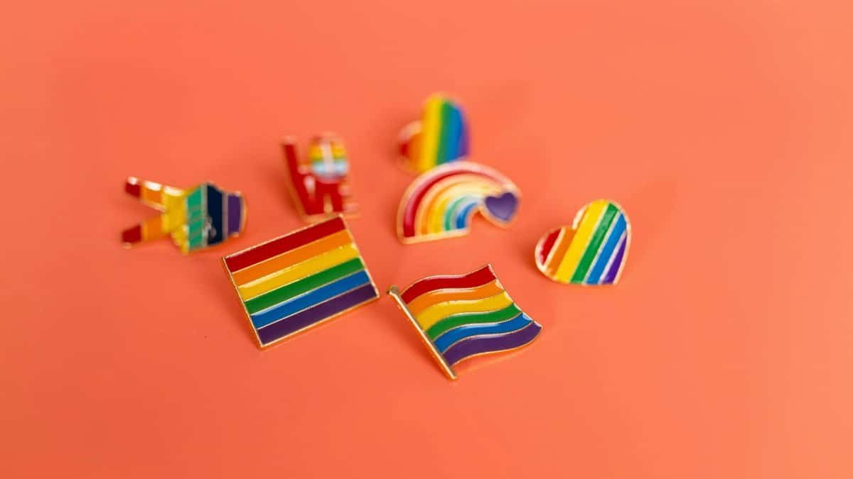 A vibrant collection of LGBT pride pins featuring rainbow flags and symbols on an orange backdrop.