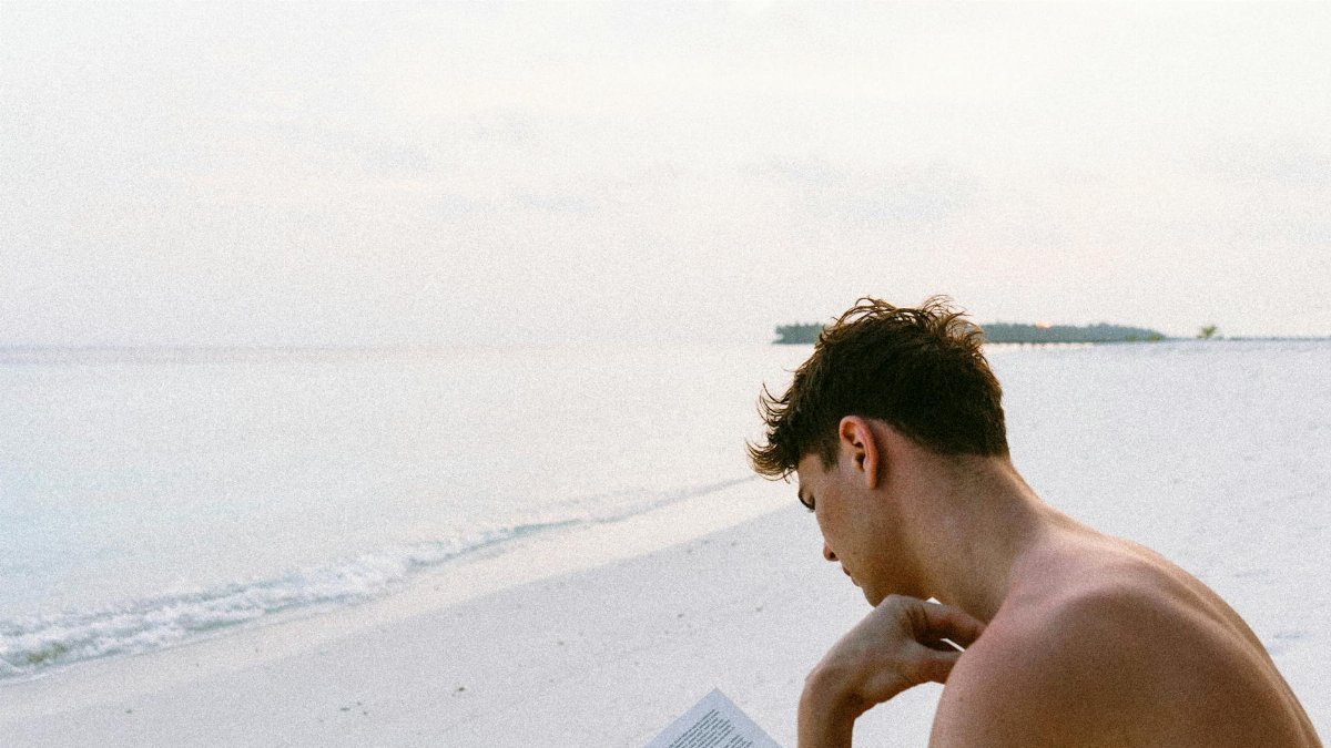A man enjoys reading a book on a serene Maldives beach, capturing the essence of relaxation.