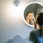 A woman applies under eye patches in a modern bathroom, emphasizing self-care.