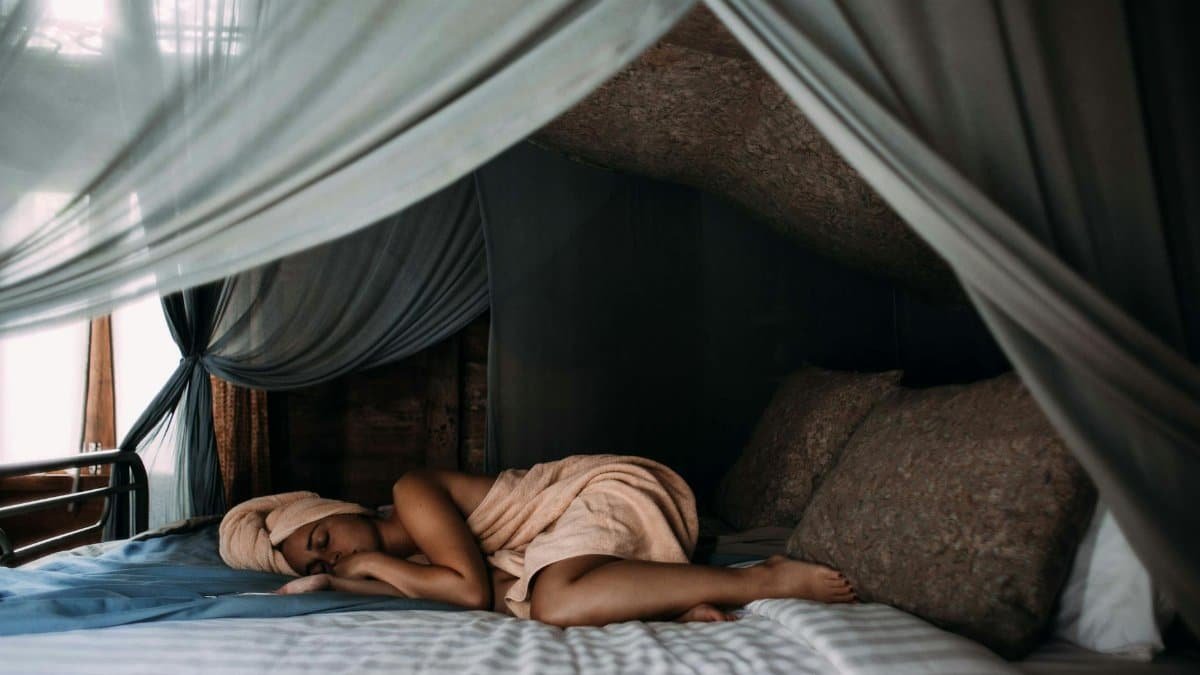 A woman rests peacefully on a cozy bed with sheer canopy curtains, creating a tranquil indoor retreat.