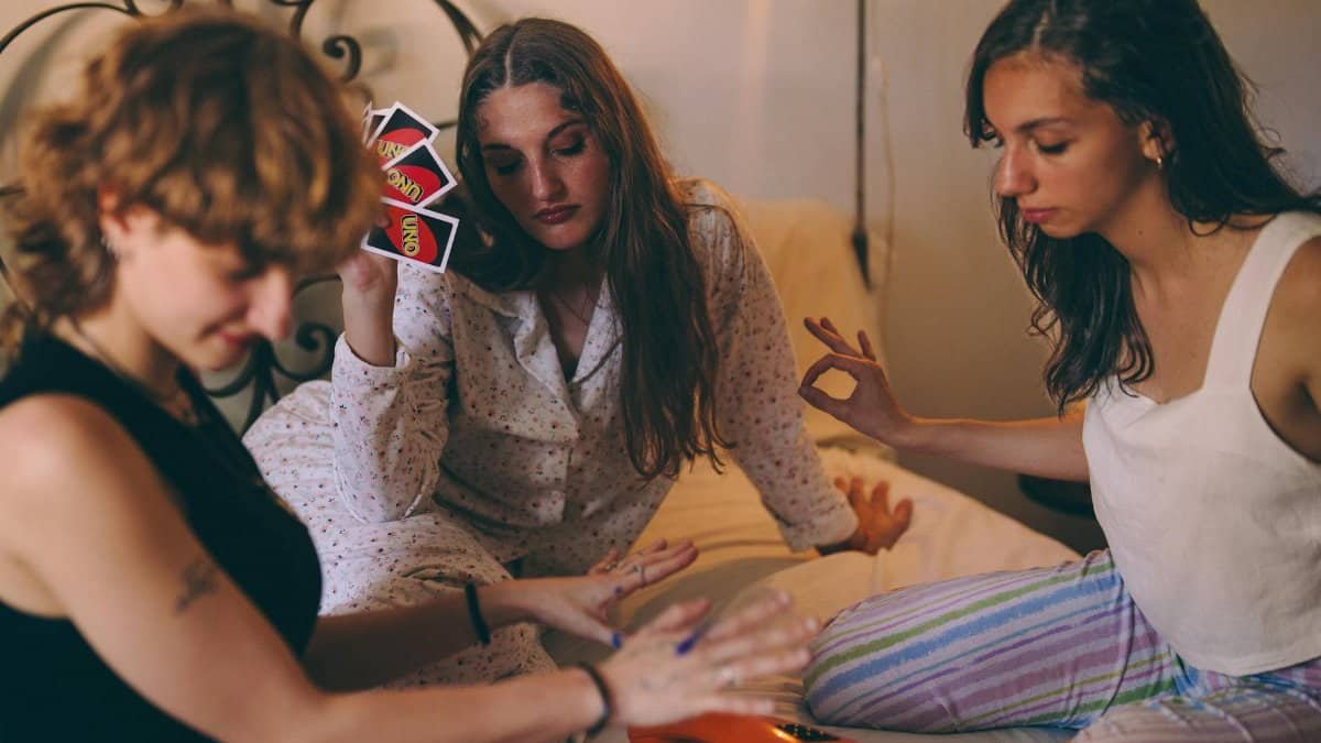 Three young women playing cards on a bed, enjoying leisure time indoors.