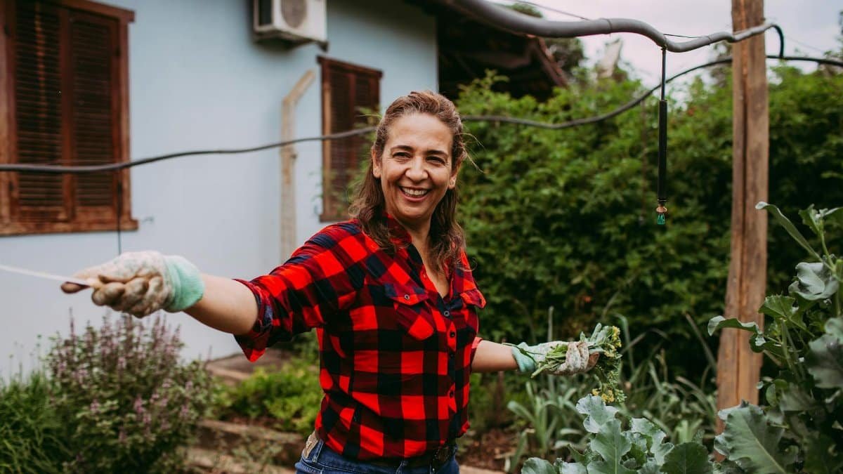 A happy woman in plaid shirt tends her garden, showcasing a vibrant, serene outdoor lifestyle.