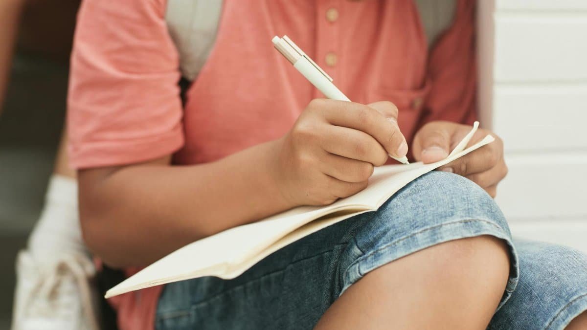 A teenager sitting outside writing in a notebook, symbolizing summer education and creativity.