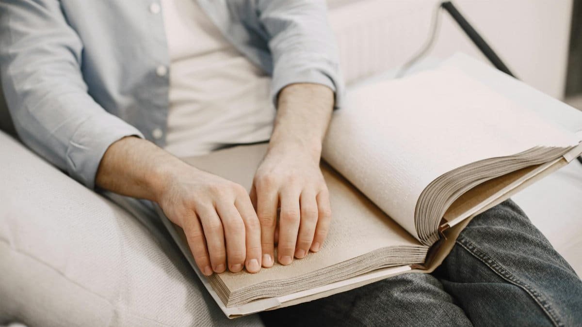 An adult reading a braille book indoors, highlighting visual impairment awareness.