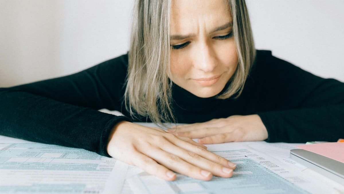 A worried woman analyzing financial paperwork at her desk, signifying stress during tax season.