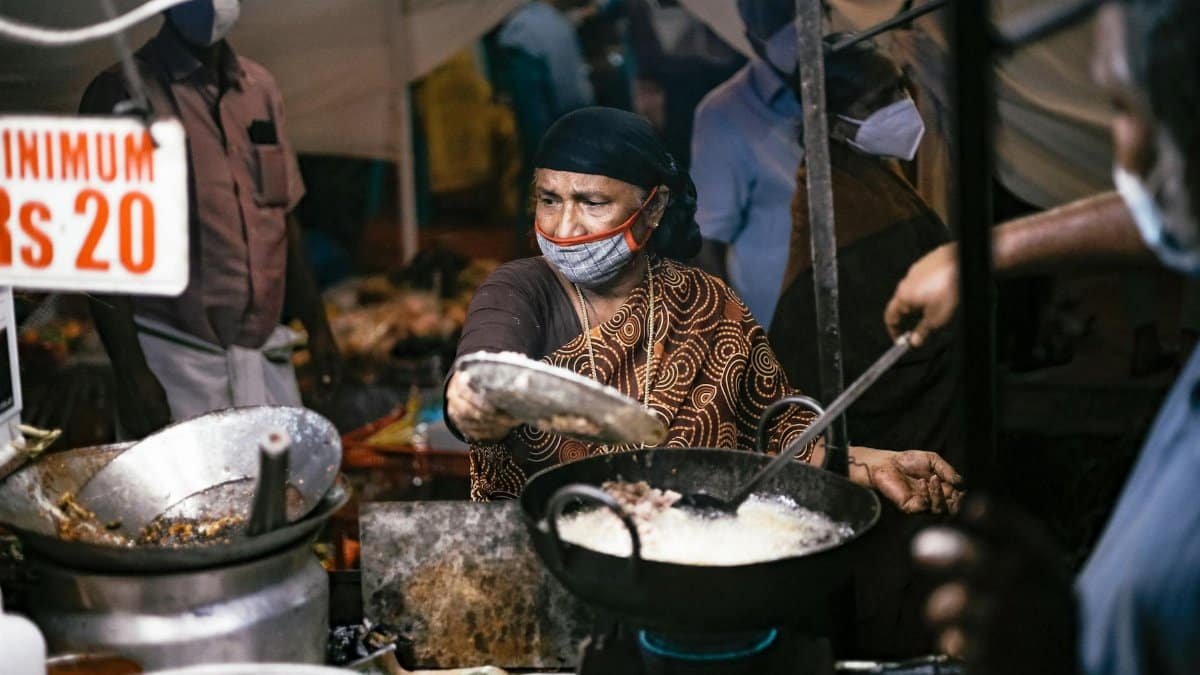 Elderly woman frying food at a bustling night market, showcasing traditional street food preparation.