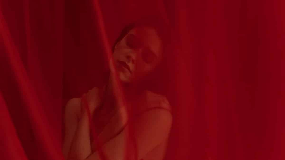 Artistic portrait of a woman with eyes closed surrounded by red curtains.