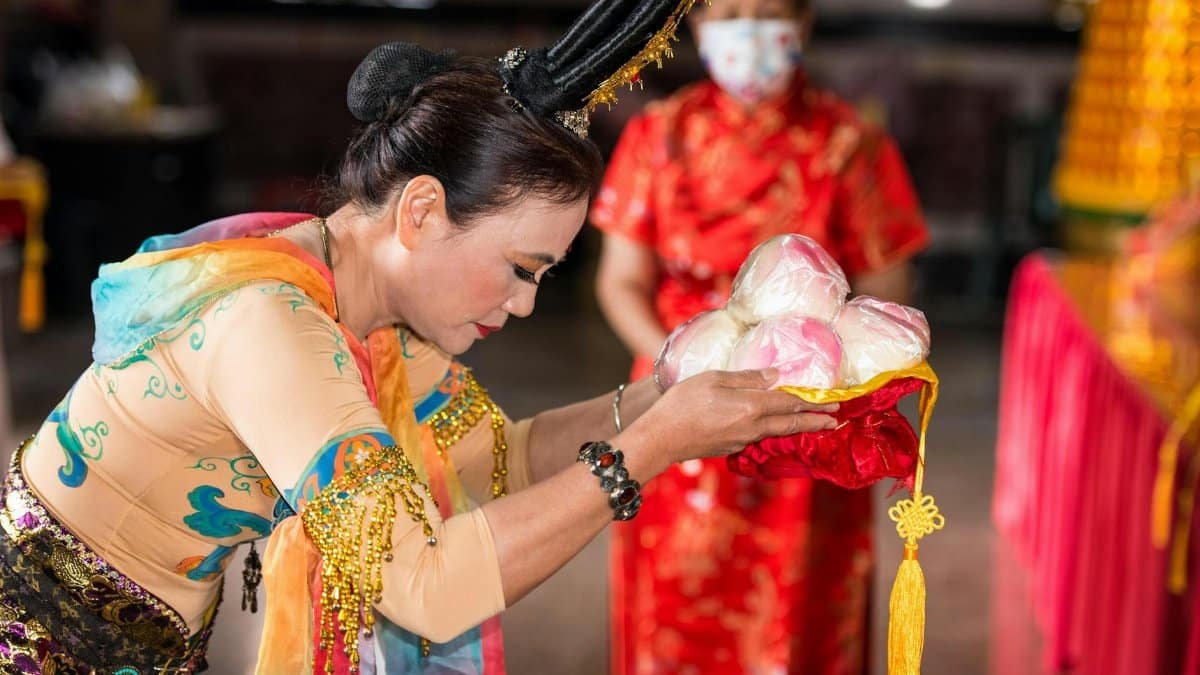 Woman in traditional clothing performs a cultural ceremony, offering fruits with reverence.