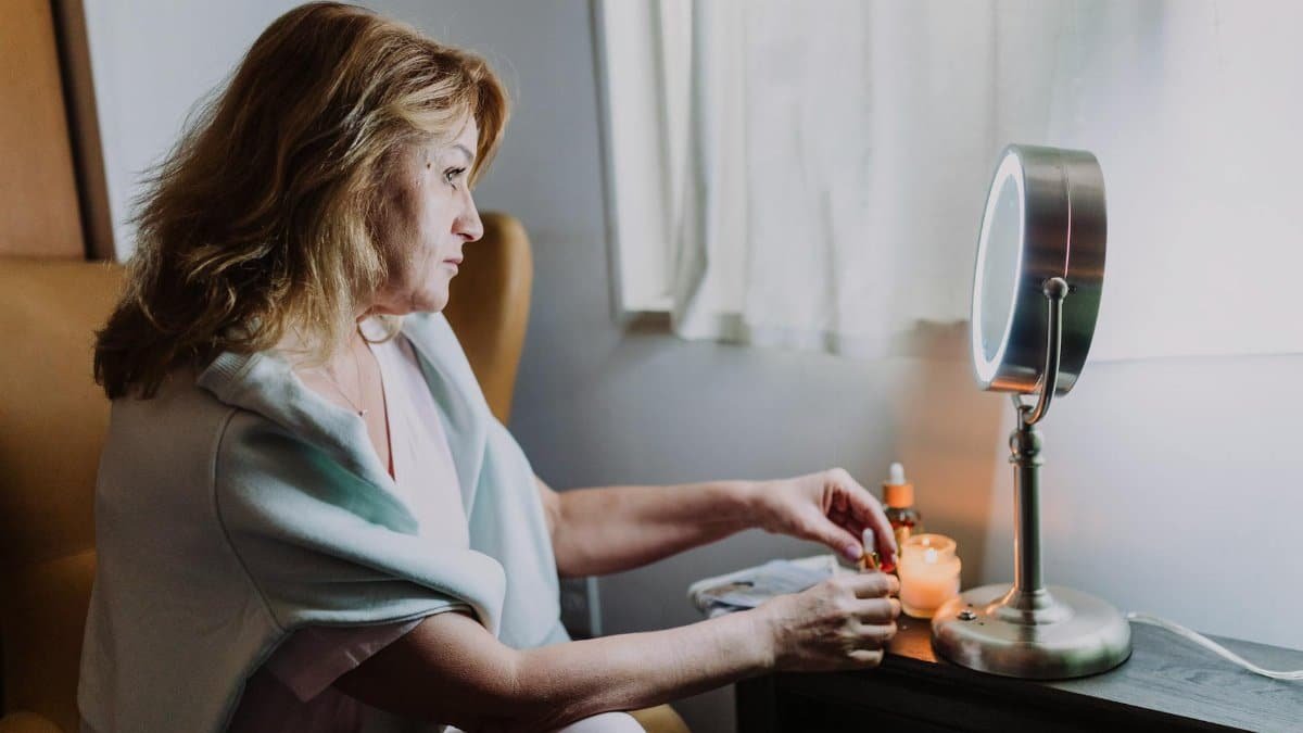 A woman enjoys a peaceful skincare routine with candles by a window.