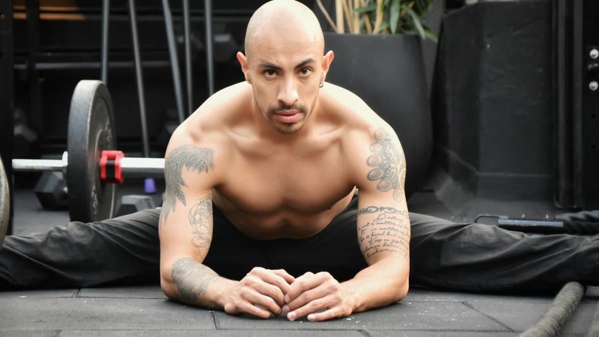 Bald man with tattoos stretching in gym, showcasing strength and flexibility.