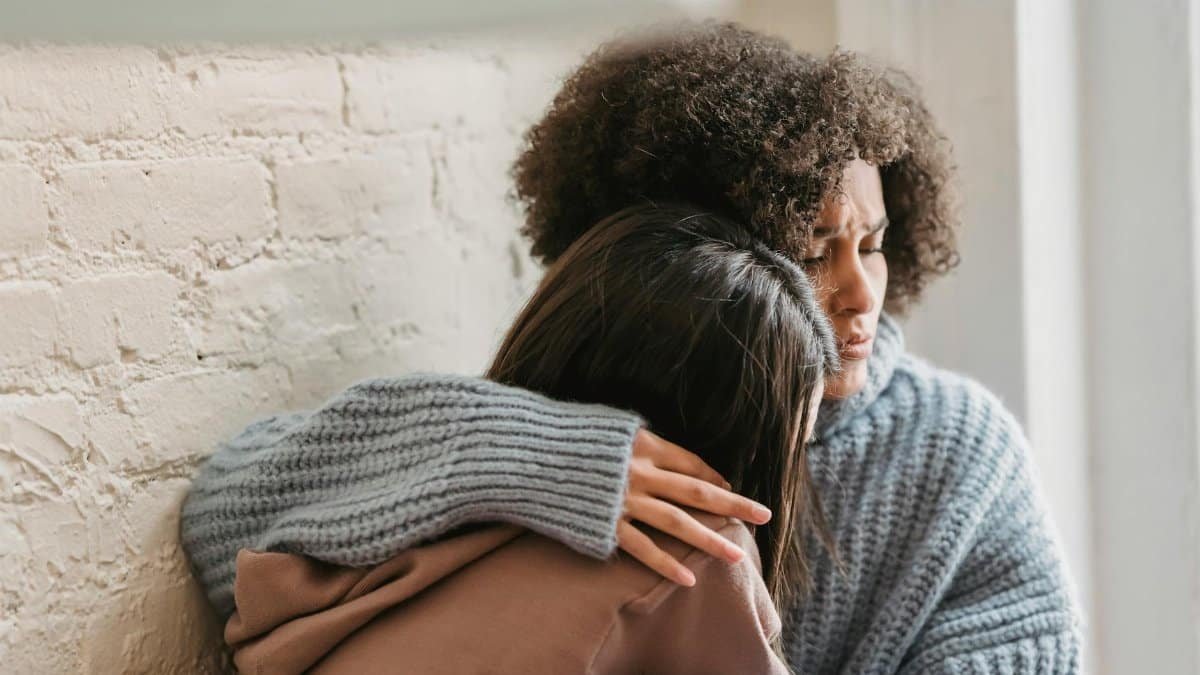 Two women hugging indoors, providing emotional support and comfort in a cozy setting.