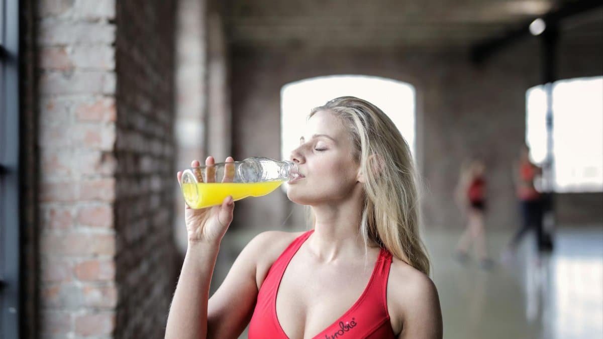 Athletic woman enjoying a refreshing drink in a gym environment, promoting fitness and hydration.