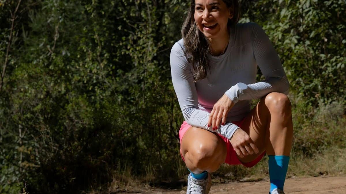 Smiling woman in sportswear takes a break during an outdoor workout, surrounded by nature.