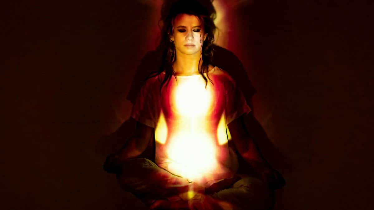 A woman in meditation surrounded by a radiant aura, symbolizing spiritual energy and enlightenment.
