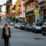 Vibrant Chinatown street featuring red lanterns, people, and parked cars on a bright day.