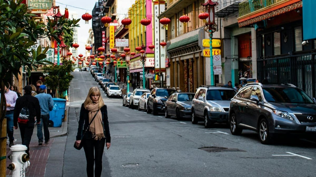 Vibrant Chinatown street featuring red lanterns, people, and parked cars on a bright day.