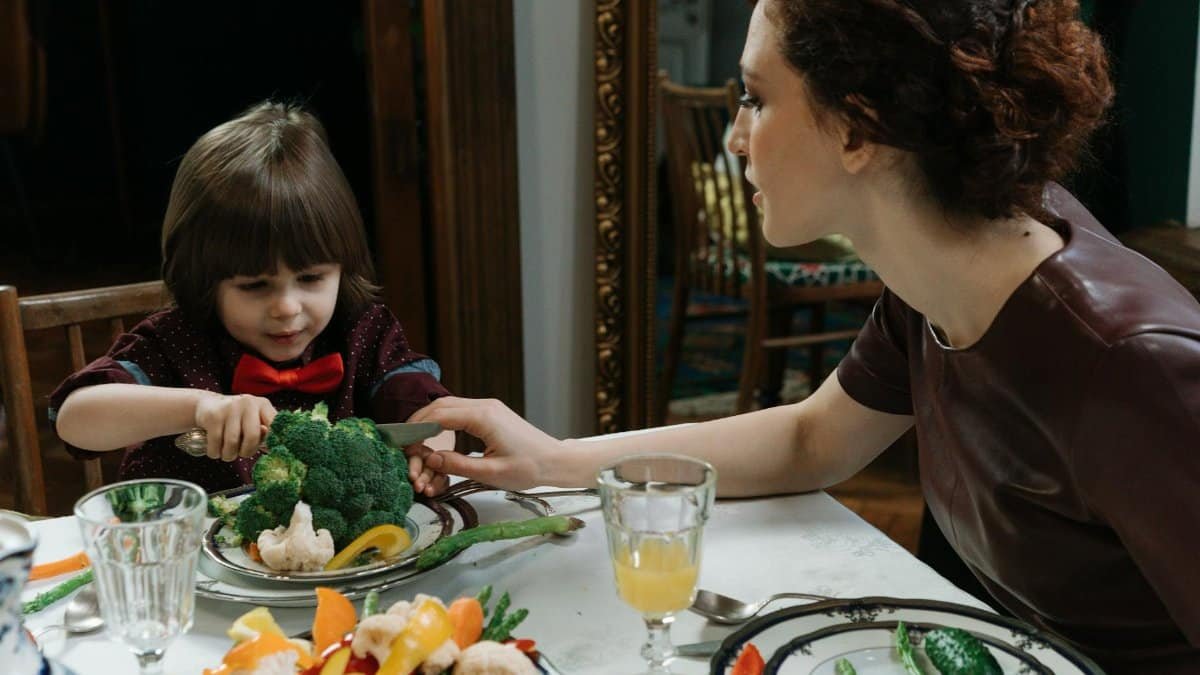 A young boy and a woman sharing a meal with vegetables, promoting healthy eating habits.