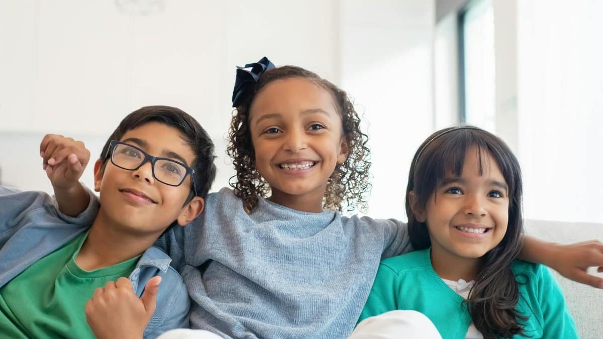Three cheerful children sitting closely on a sofa, smiling joyfully.